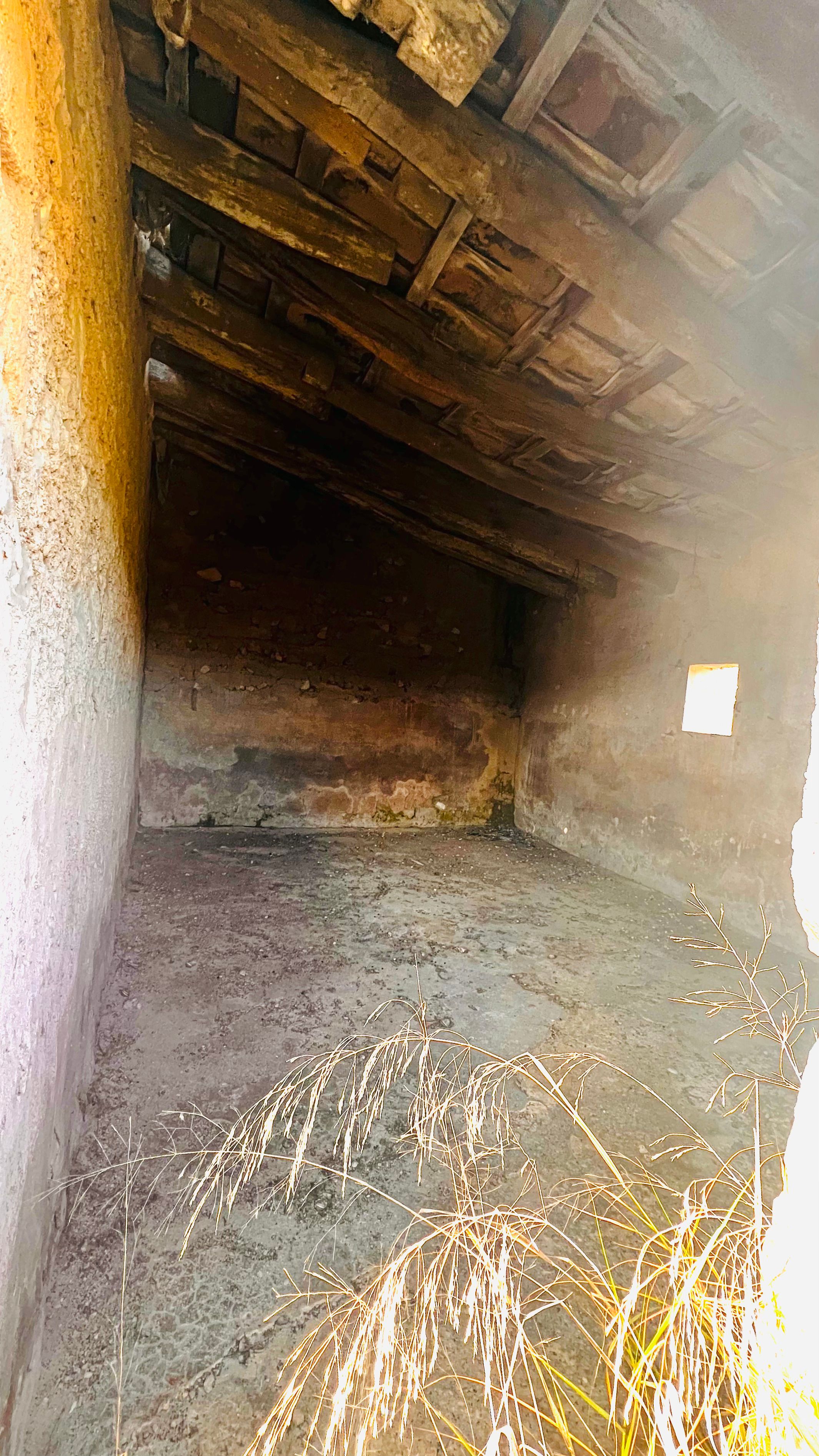 An old, dilapidated interior with a wooden ceiling and floor covered in hay or straw.