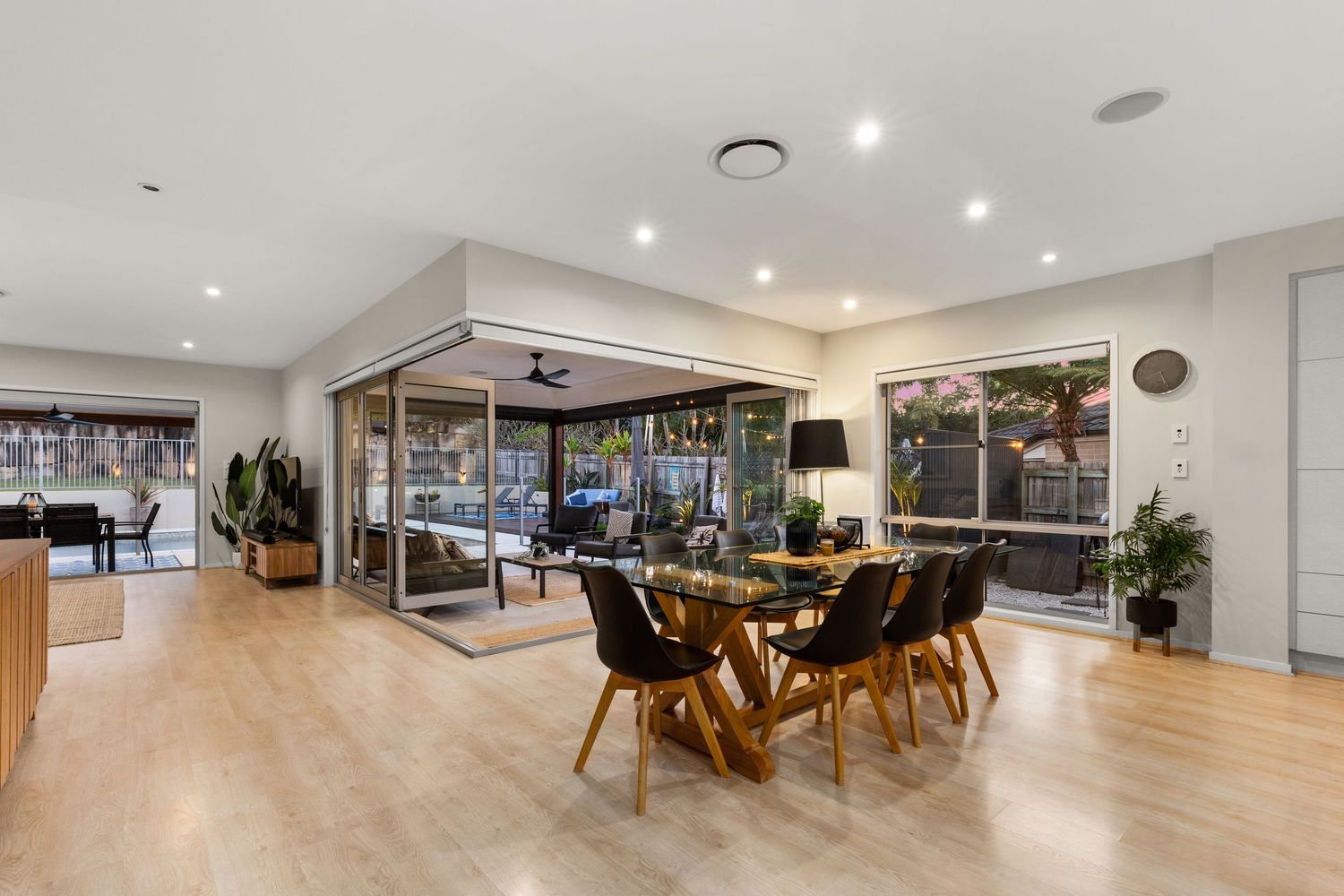 Bright open-plan dining and living area with timber floors, recessed lighting, and large glass sliding doors.