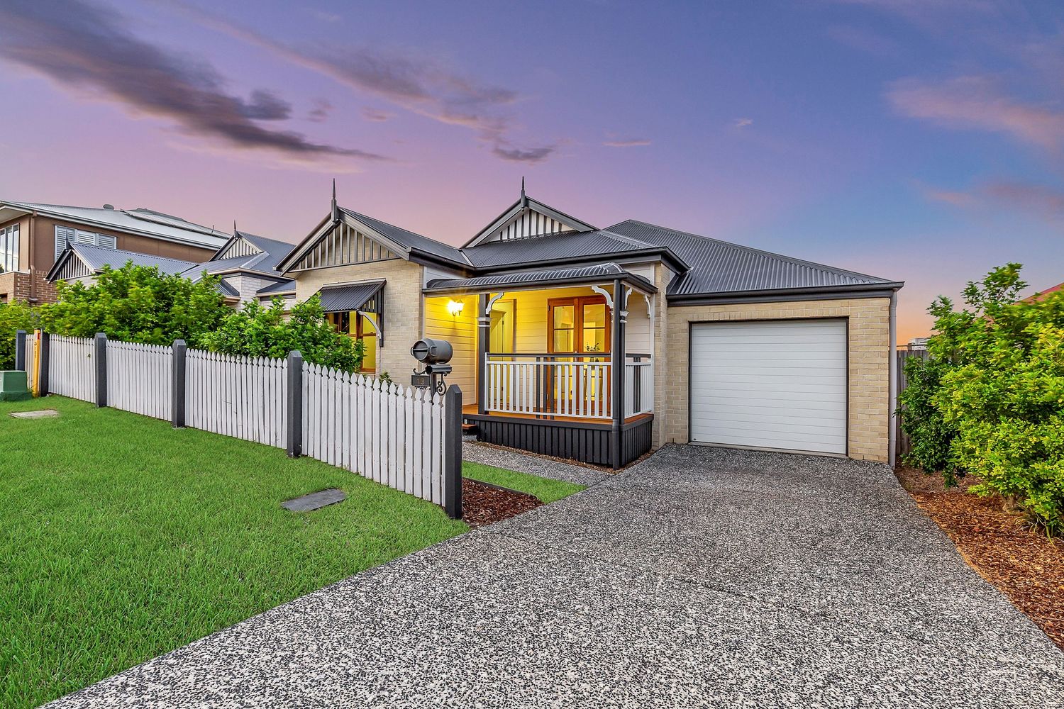 Charming Queensland home with white picket fence, manicured lawn, covered porch, and double garage at twilight.