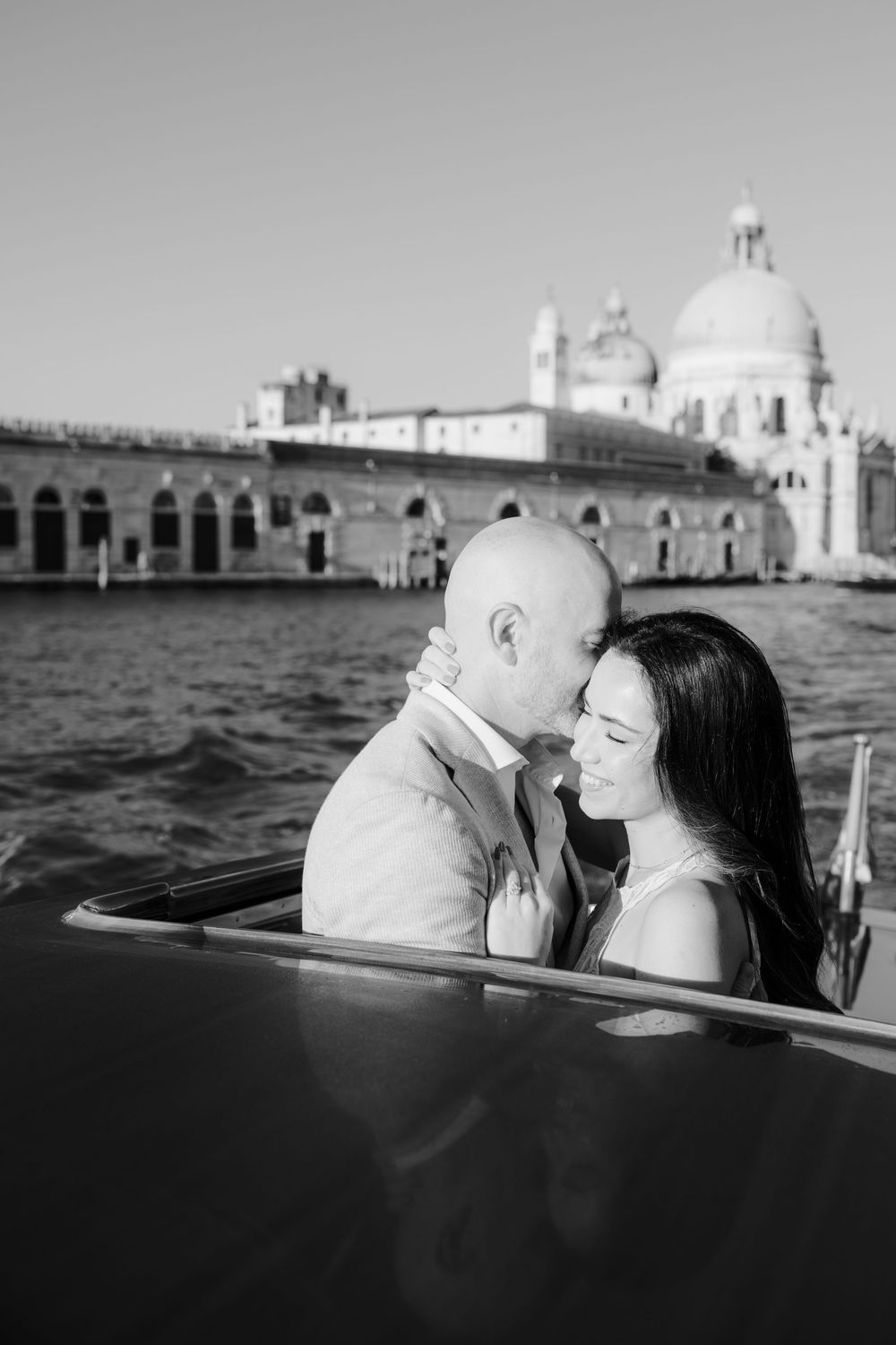 Romantic black and white sequence of a couple sharing intimate moments on a boat in Venice with historic buildings in background.