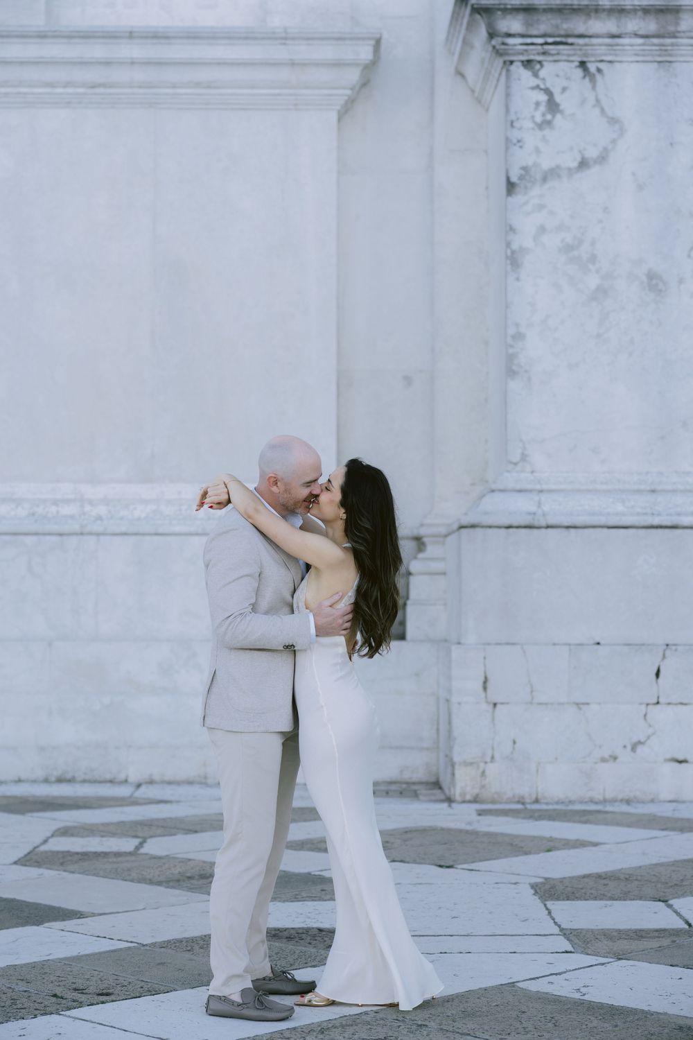 Two dancers in white outfits perform a contemporary duet against a marble wall backdrop.