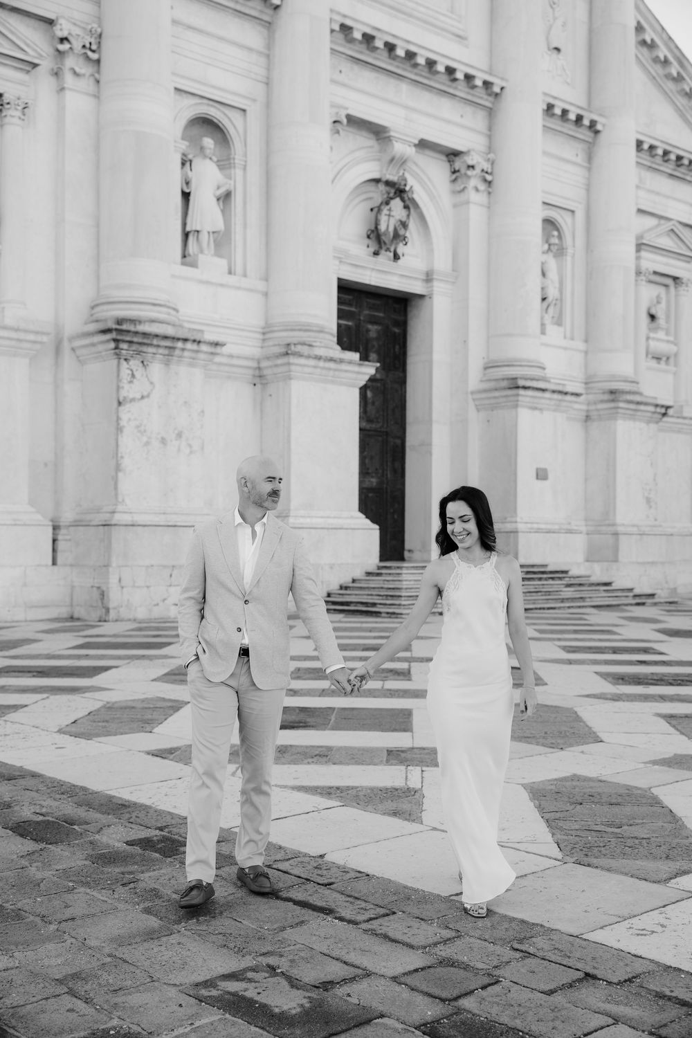 Black and white wedding photo of a couple walking down stone steps in front of an ornate white church facade.