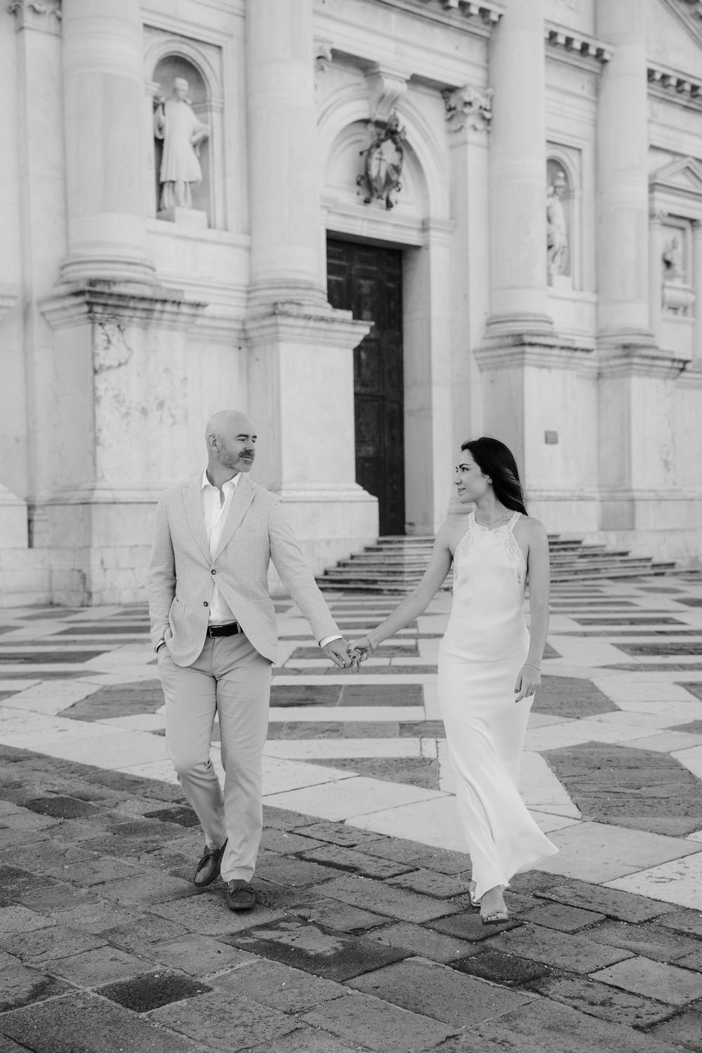 A romantic black and white wedding photo series showing a couple walking together through an elegant columned building.