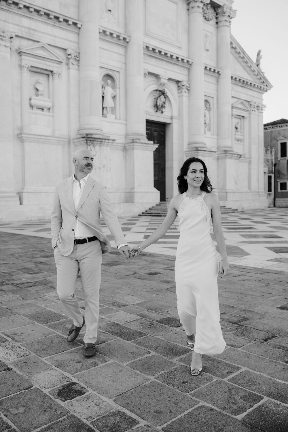 A series of black and white photos showing a couple in white outfits dancing and posing in front of a grand white building.