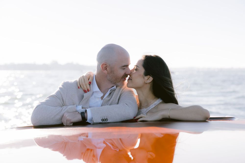 A couple shares a tender moment lying together on a white blanket at the beach.