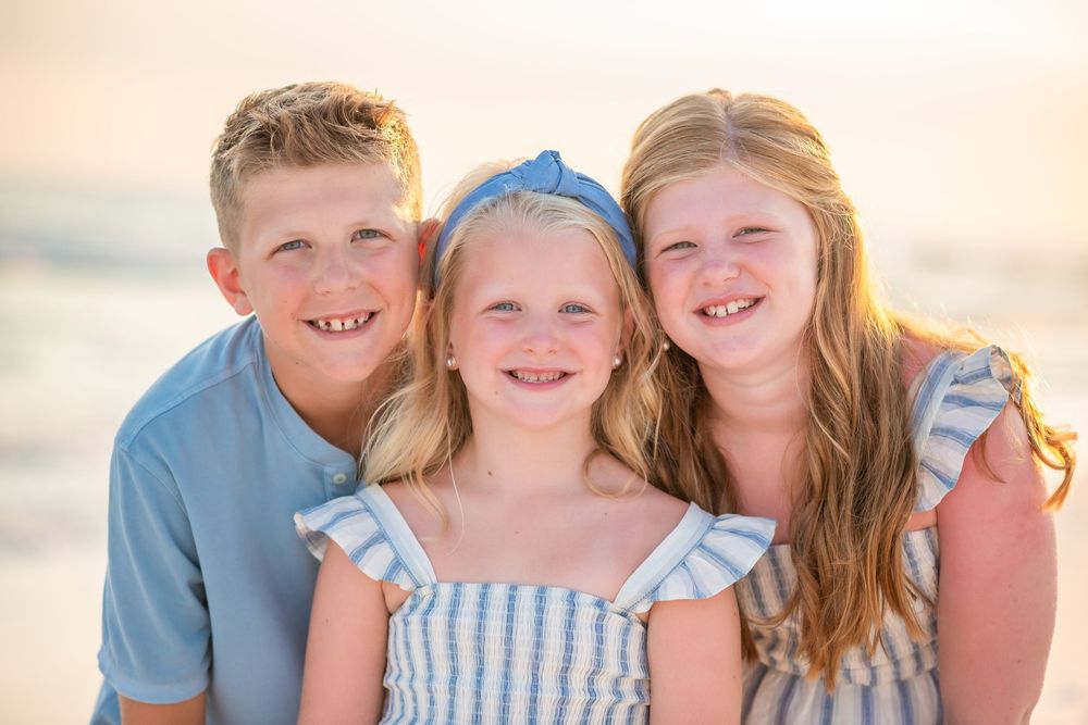 Family enjoying a sunset photoshoot on the beach wearing coordinated blue and white outfits.