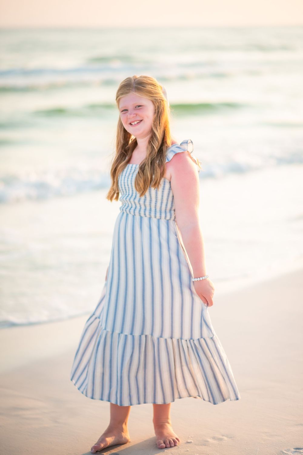 A beachside portrait featuring a blue and white striped summer dress against ocean waves.