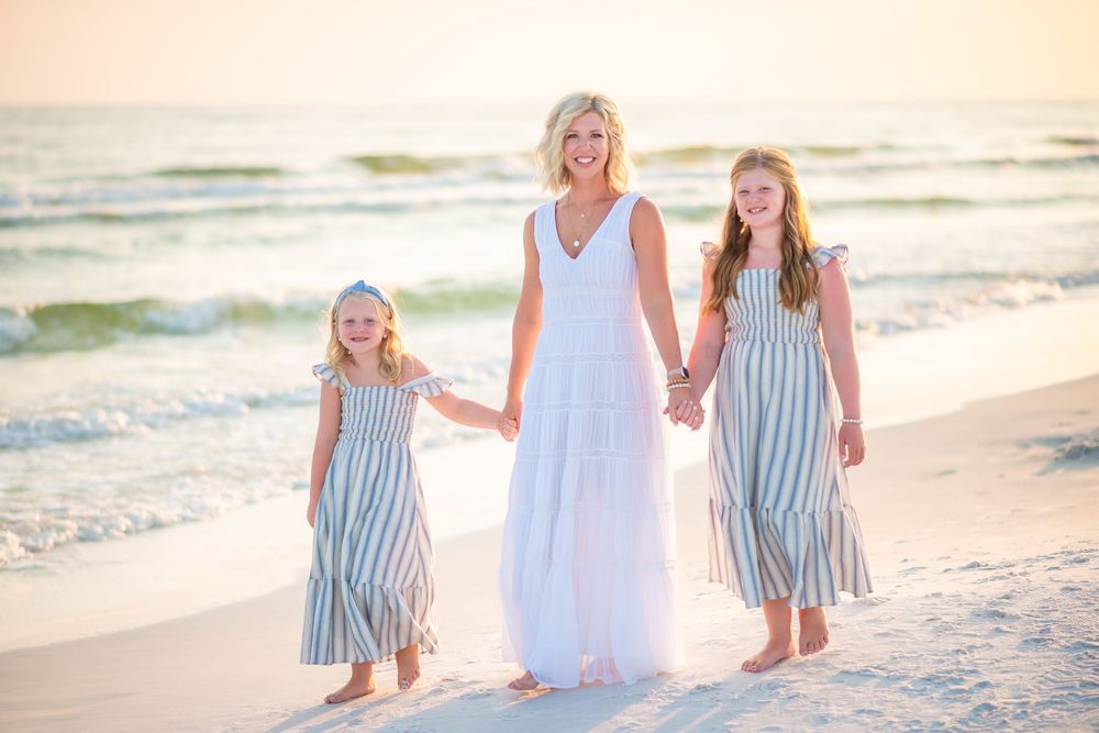 Family walking together on a sunny beach wearing coordinated white and blue striped outfits.