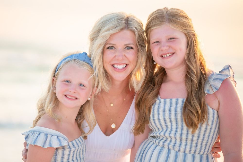 Three people in coordinating blue and white outfits pose together on a sunny beach.