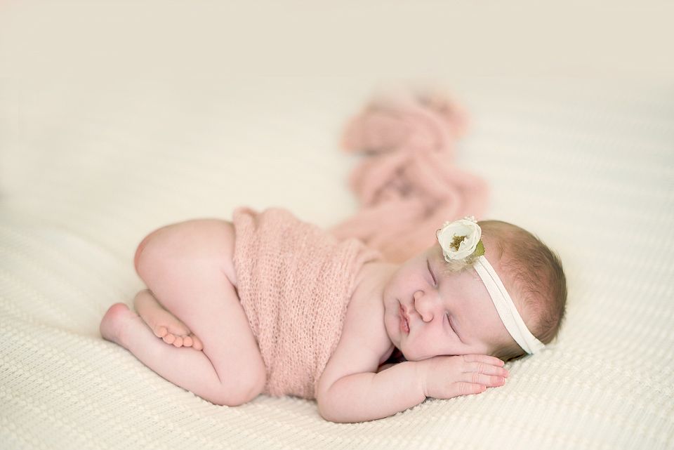 A collage of four images showing a sleeping newborn baby wearing pink clothing on white textured fabric.