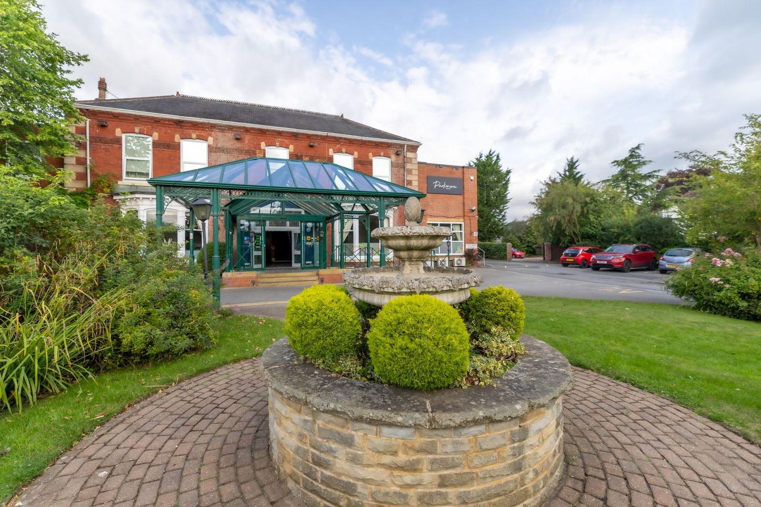 A curved stone pathway leads through landscaped gardens with green shrubs and brick buildings in the background. Parkmore Hotel Wedding