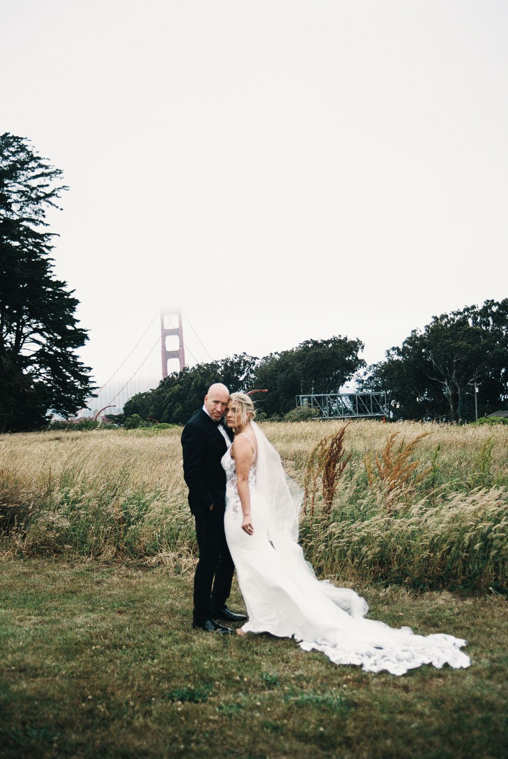 Bride and groom embrace in golden grass field with Golden Gate Bridge backdrop in San Francisco.