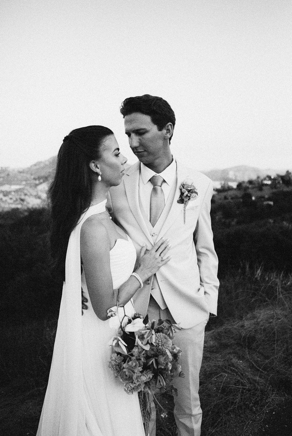 Black and white photo of a bride and groom sharing an intimate moment outdoors with hills in the background.