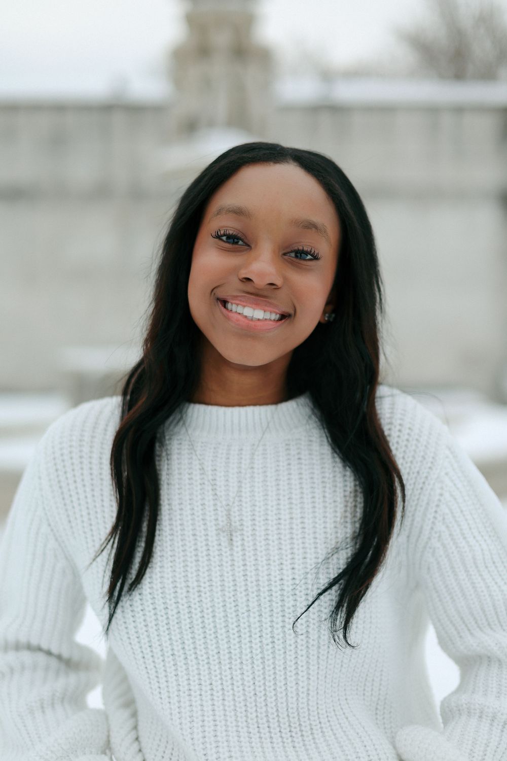 A cheerful winter portrait featuring a white knit sweater and long dark hair.