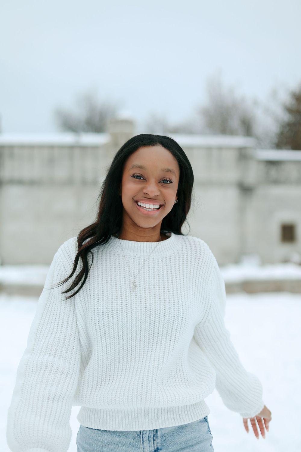 A person wearing a cozy white knit sweater smiles brightly against a snowy winter backdrop.
