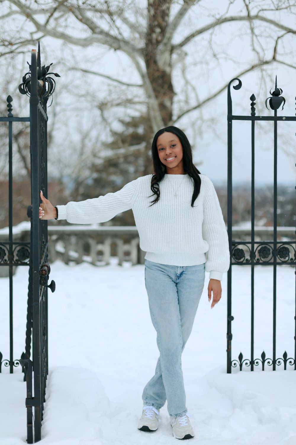 Casual winter outfit showcased against ornate iron gate in snowy setting.
