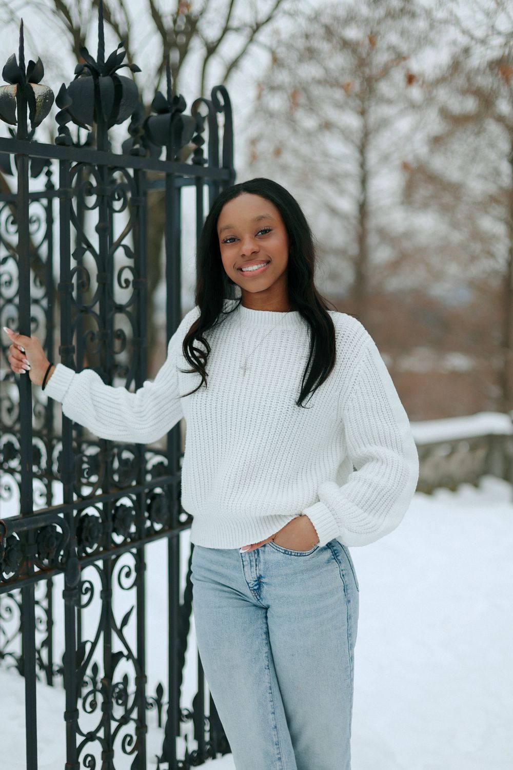 Casual winter style portrait against ornate iron gate in snowy setting.