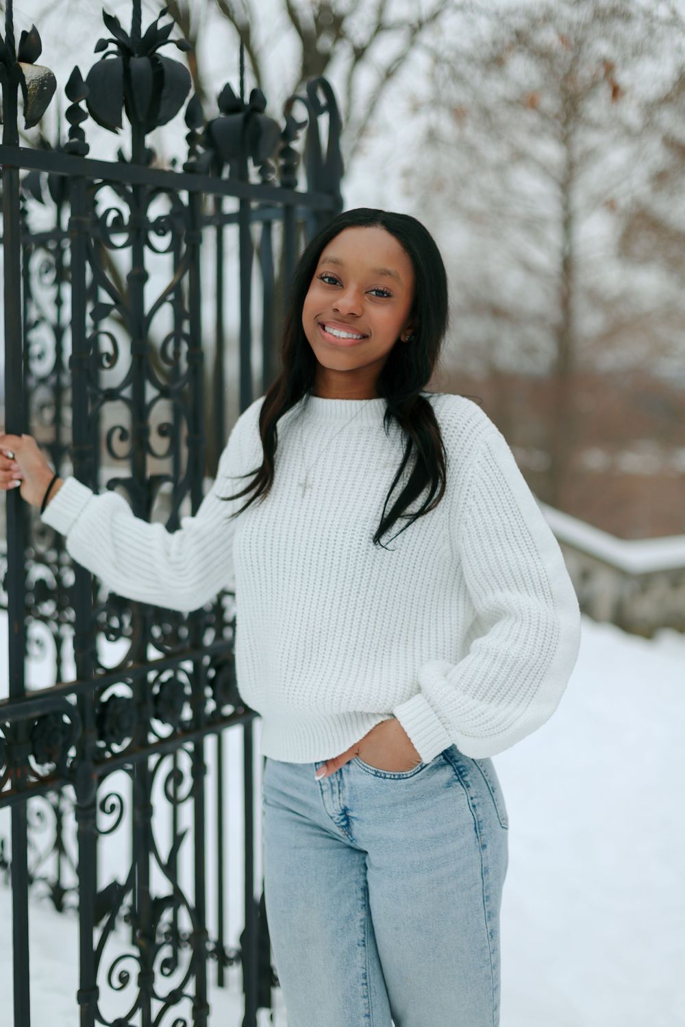 Playful winter pose by decorative iron gate in casual white and denim outfit.