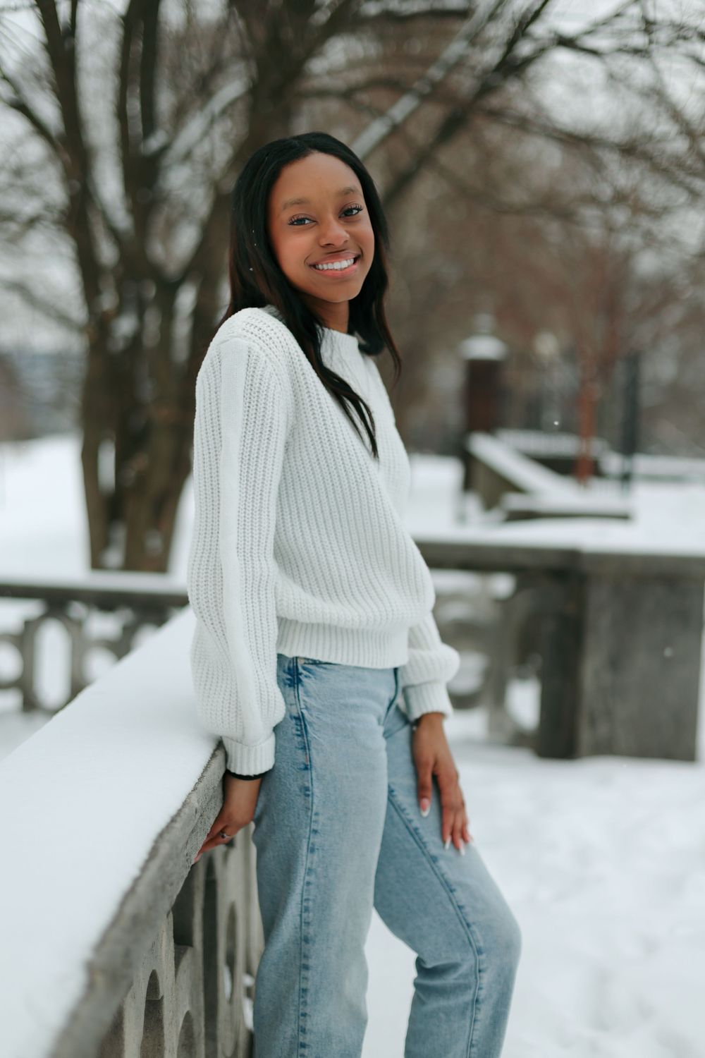 Casual winter style with white ribbed sweater and jeans against snowy outdoor setting.