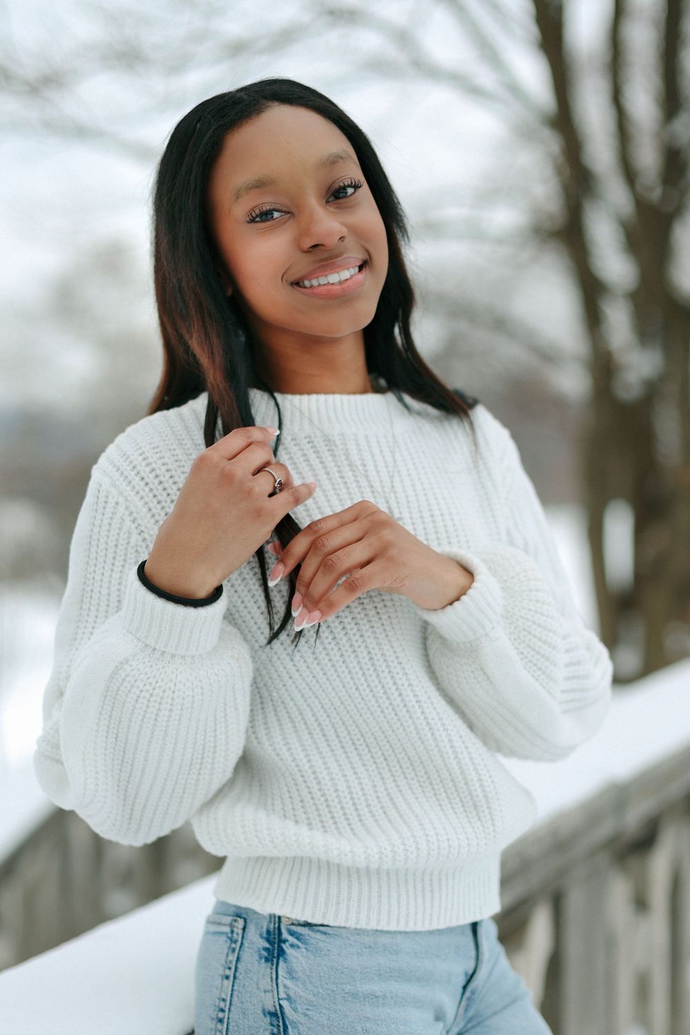 A winter portrait featuring a white knit sweater and light denim against a snowy outdoor backdrop.