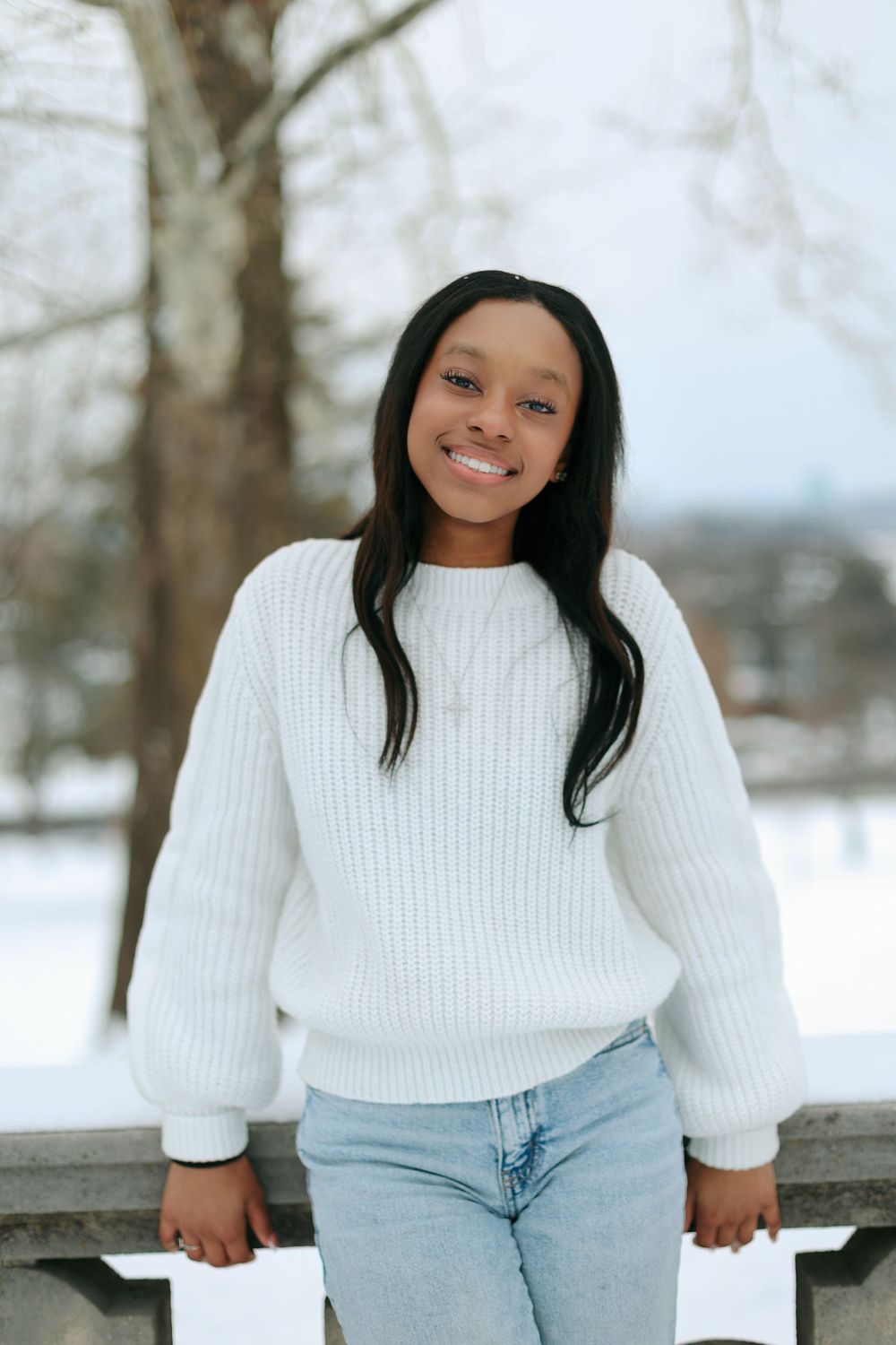 Winter fashion portrait on a snowy ledge wearing classic denim and white sweater combination.