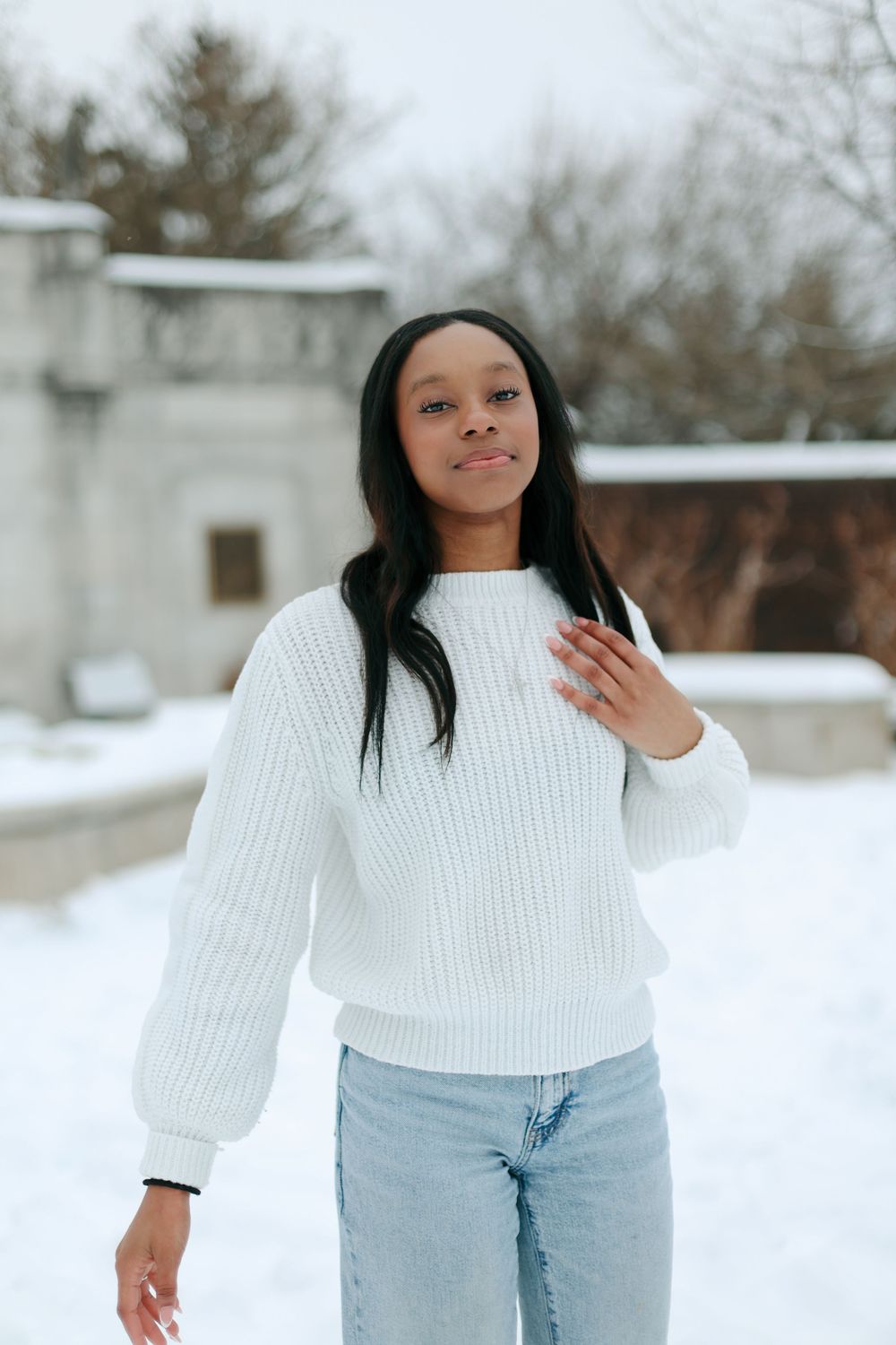 Someone in casual winter attire poses against a snowy backdrop with trees.