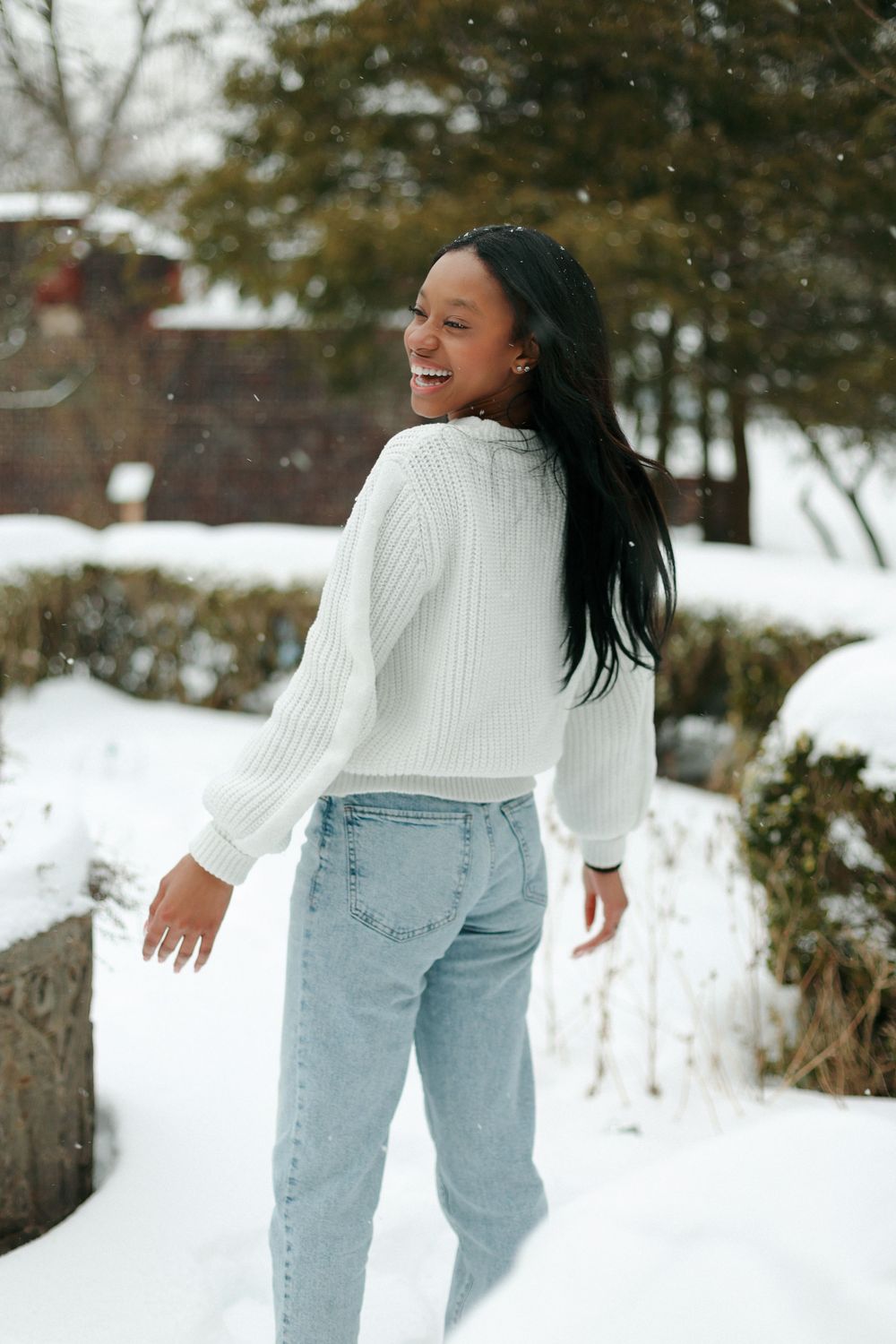 A winter portrait showing a cozy white sweater and light jeans against a snowy background.