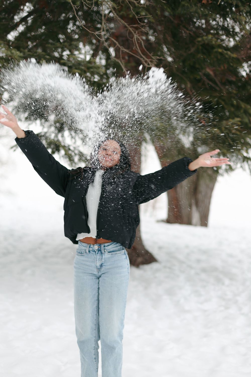 Playful winter scene with snow being tossed while wearing casual denim and white sweater.