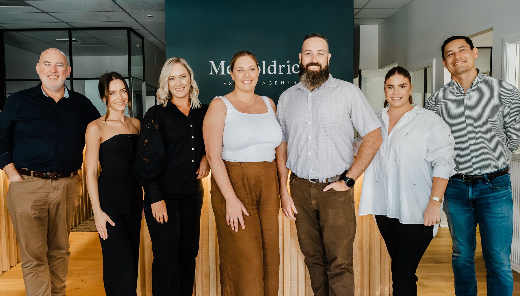 A group of professionals stand together in a modern office space for a team photo.