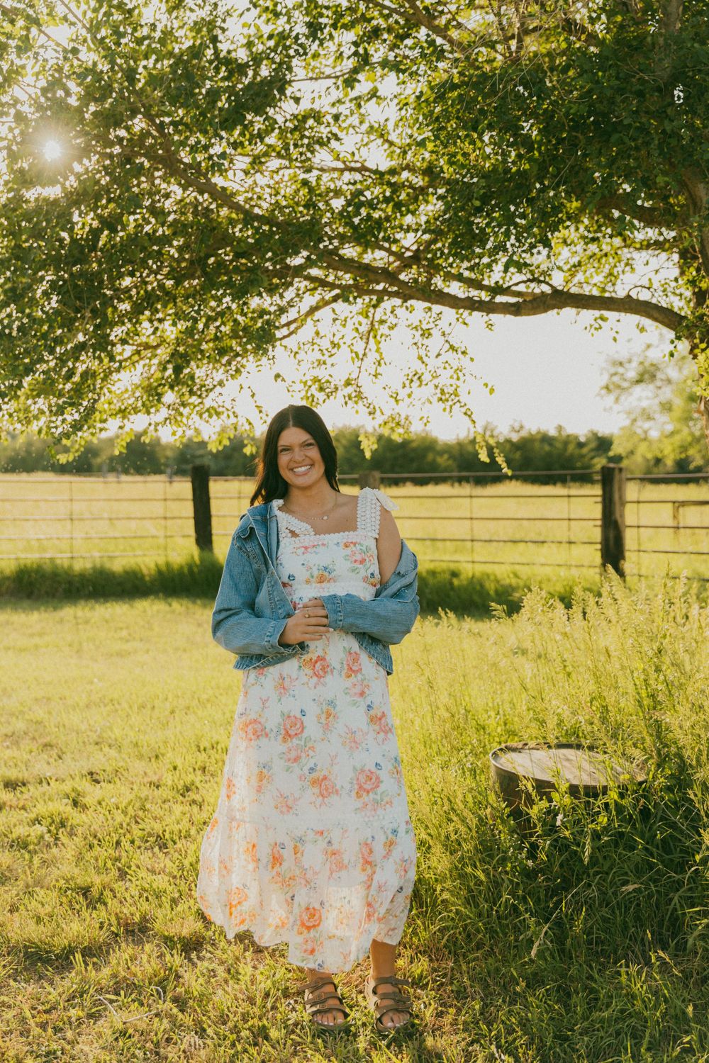 A floral dress is displayed in a sunny meadow during golden hour with trees in the background.