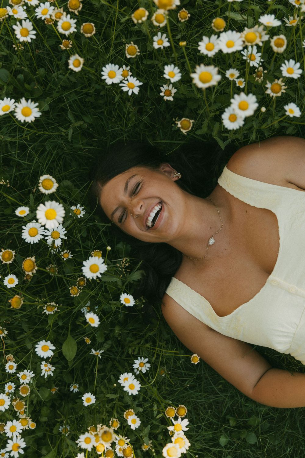 Person lying in a field of blooming white daisies wearing a white dress on a sunny summer day.
