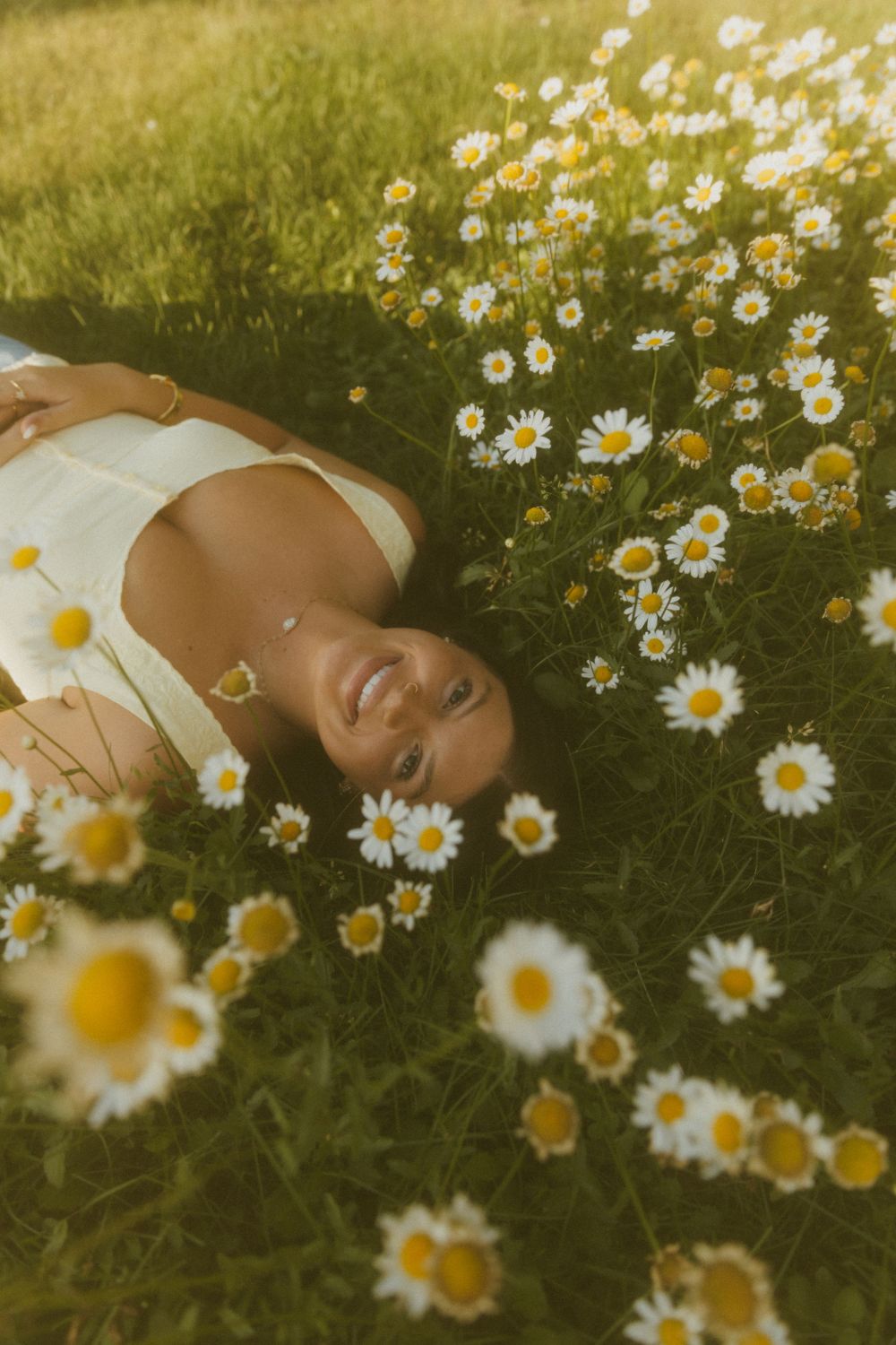 A person lies peacefully in a meadow surrounded by blooming white daisies on a sunny summer day.