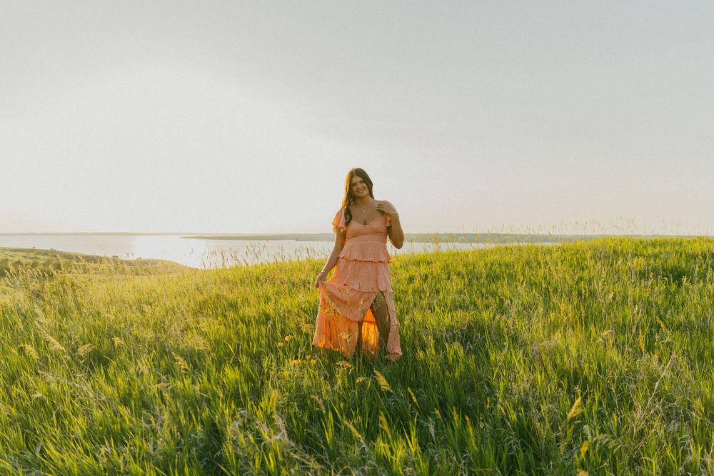 A person in a flowy dress walks through a golden field at sunset creating a dreamy silhouette against the sky.