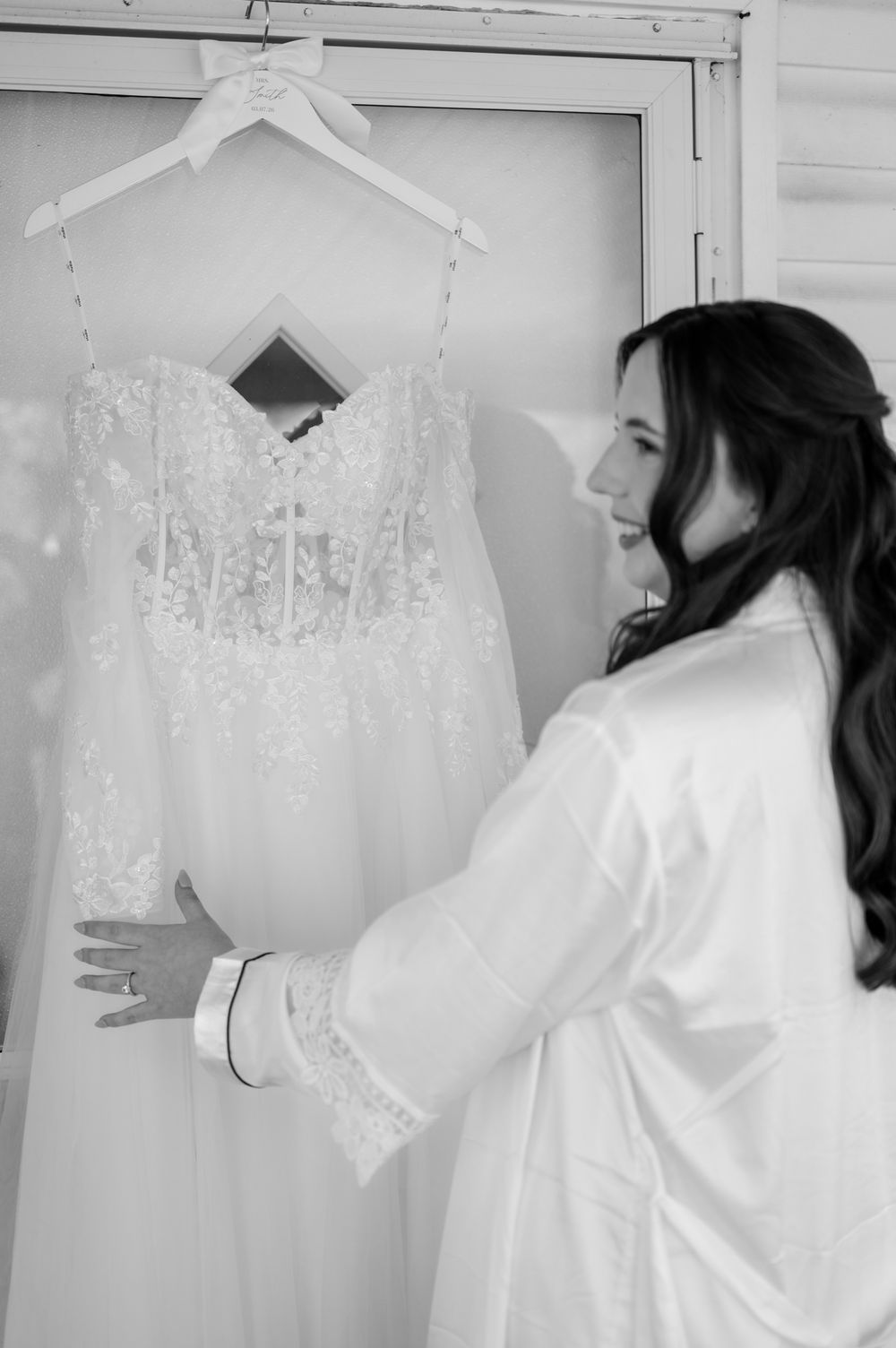 A series of white lace wedding dresses hanging on display against a light colored wall.