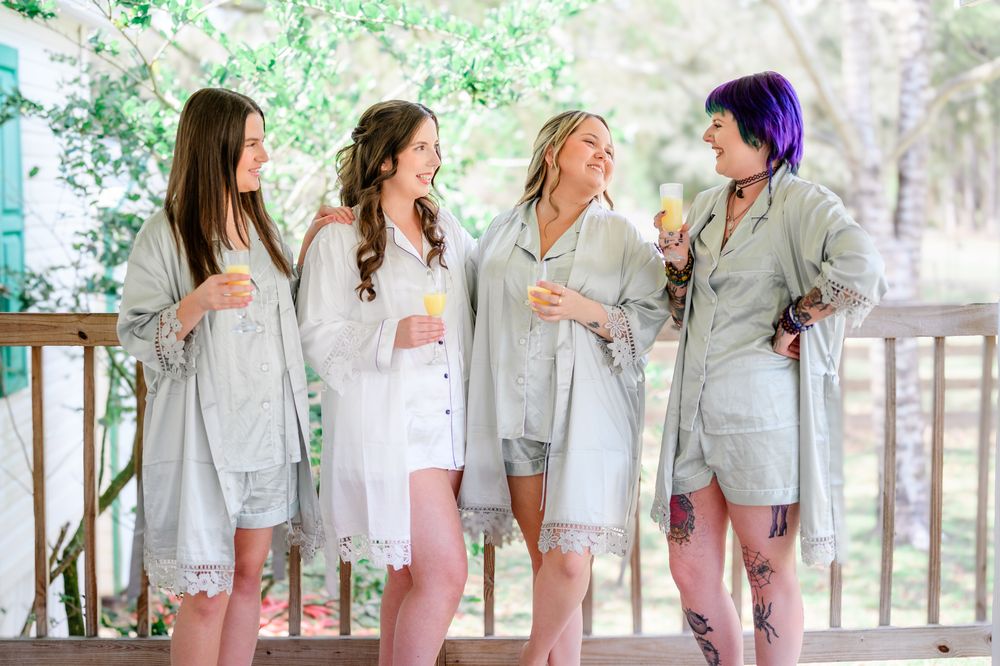 Bridesmaids wearing matching light gray robes pose together during wedding preparations.