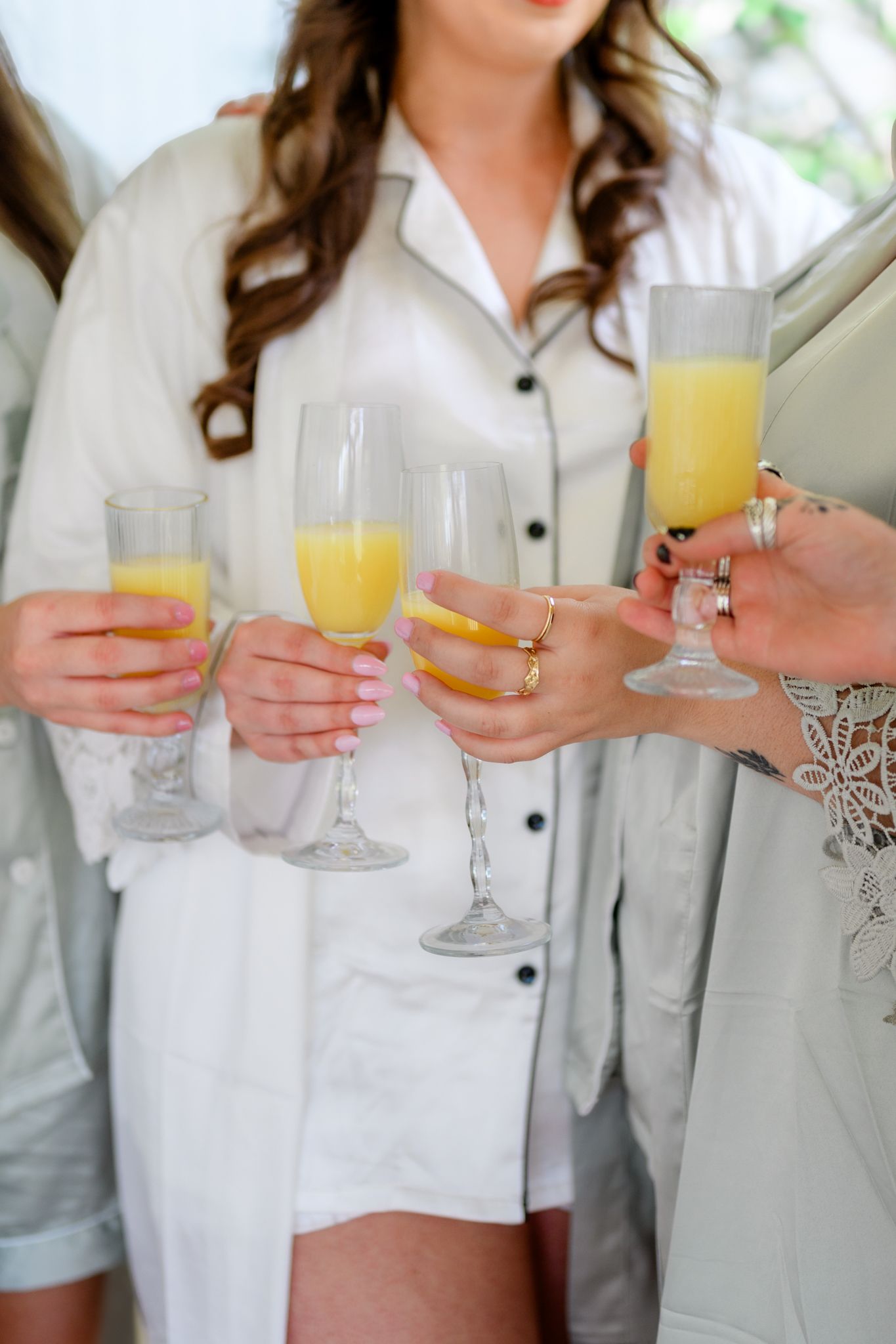 People in white and gray clothing hold champagne glasses filled with mimosas during a celebratory gathering.