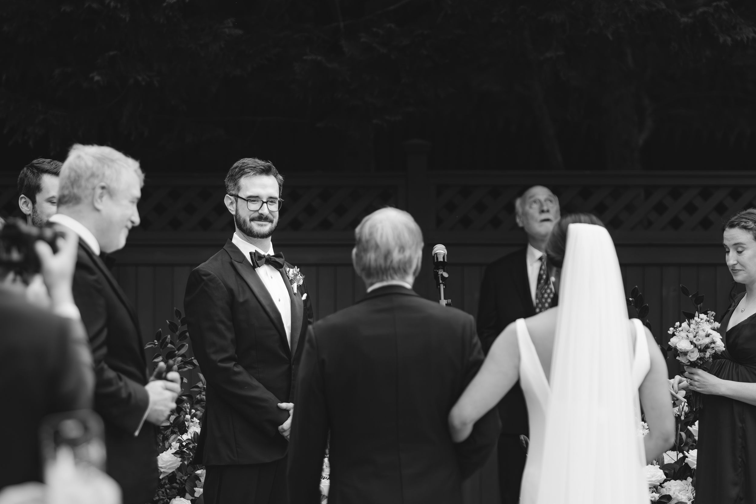 Black and white photo of a wedding ceremony in progress with the couple and officiant at the altar during an outdoor service.