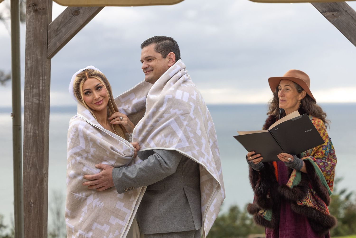 A couple embraces during a romantic outdoor photo session at a rustic wooden venue.