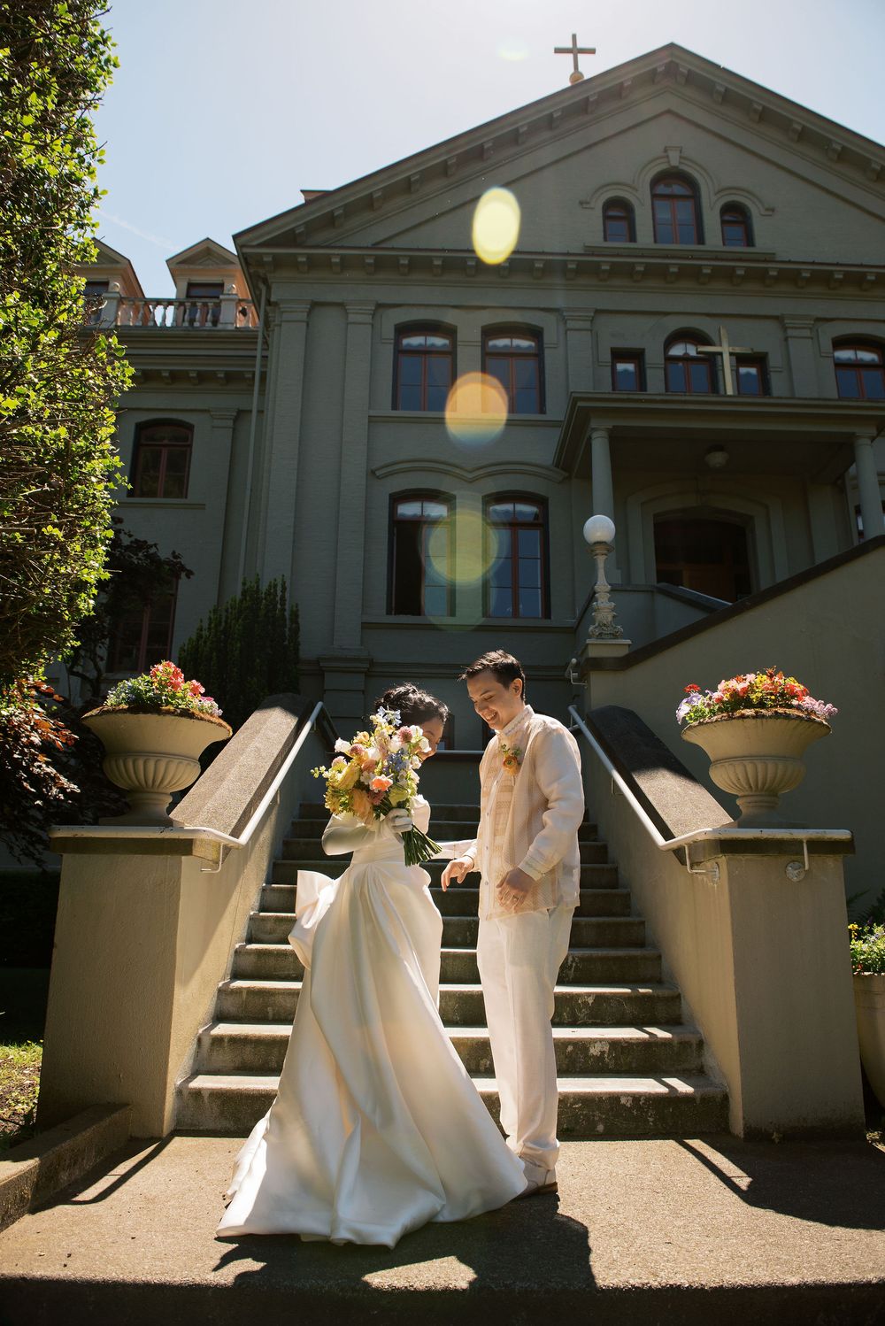 Bride and groom holding hands on church steps with colorful bouquet on sunny wedding day.