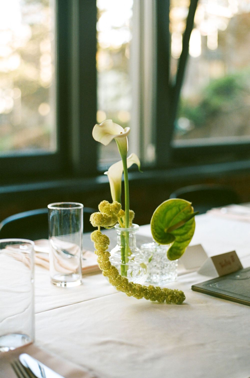Elegant wedding table centerpiece with white calla lilies, green anthurium, and textured floral accents in glass vases.