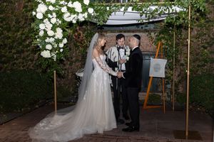 Outdoor garden wedding ceremony with white floral decorations and natural greenery.