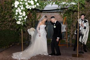 A couple in formal wedding attire performs their first dance under string lights at an outdoor evening reception.