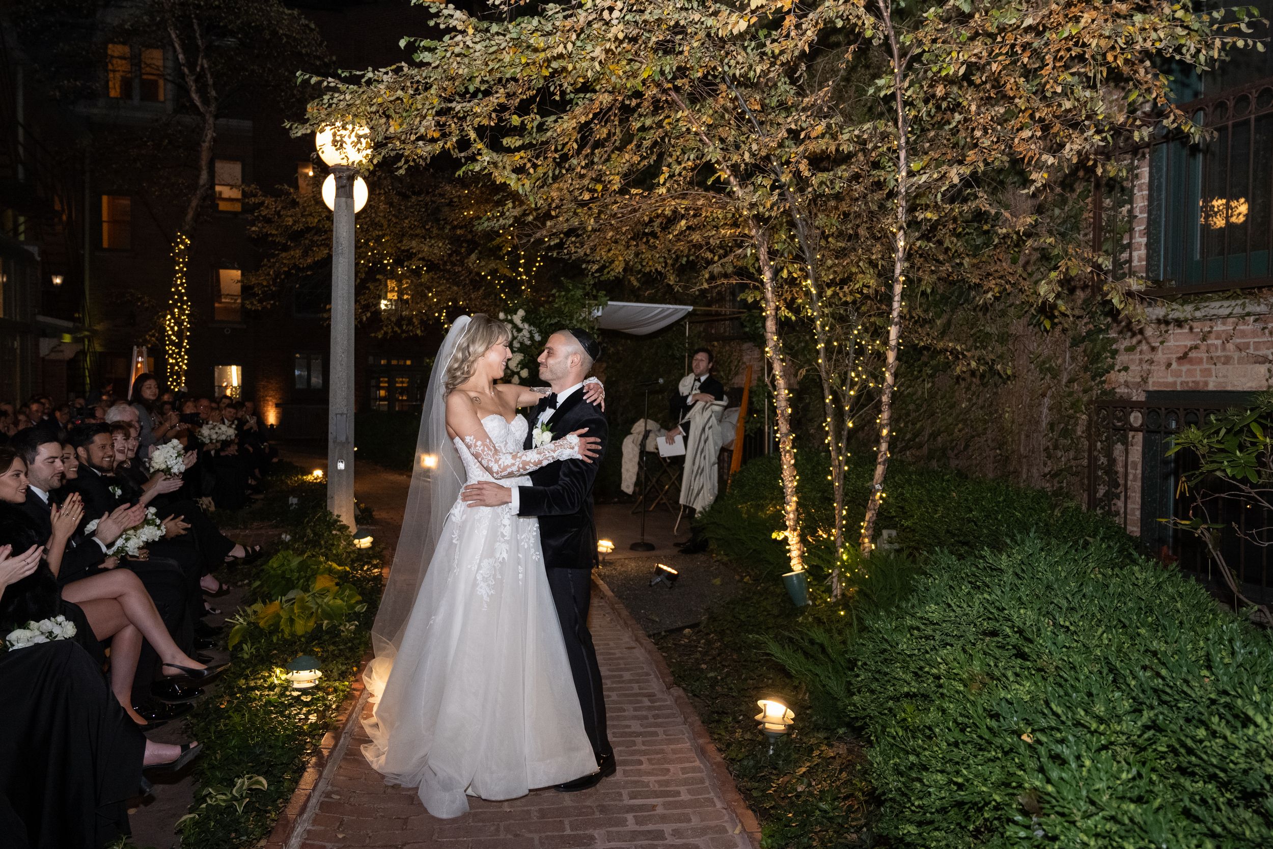 A romantic dance moment captured in a garden courtyard at dusk with soft lighting and greenery.