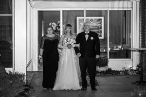 A black and white wedding photo showing a couple walking down a church hallway with guests watching from the sides.