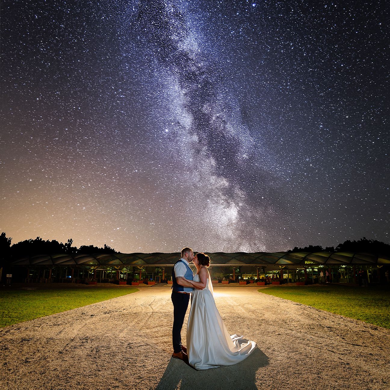 A stunning Milky Way galaxy stretches across the night sky over silhouetted figures on a dark field.