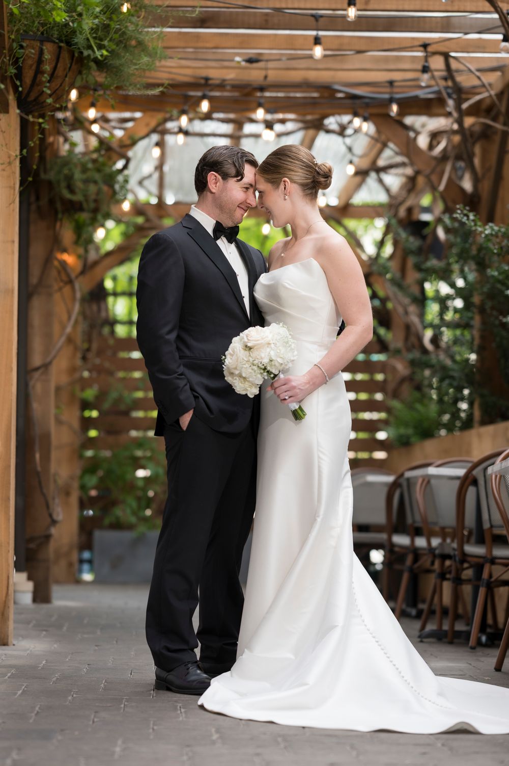 A romantic moment captured in a rustic wooden pergola setting with natural light filtering through the slats.