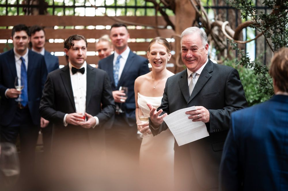 Wedding guests gather around in formal attire during a reception, sharing laughter and conversation together.