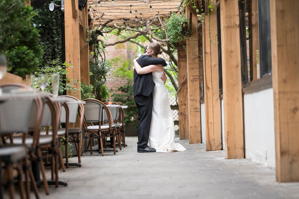 A rustic wooden colonnade walkway with stone pillars creates an elegant outdoor corridor at a wedding venue.