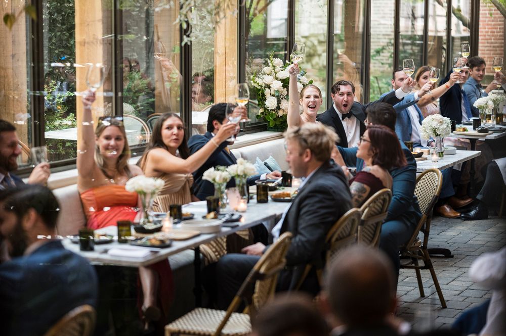 Wedding guests sit at outdoor tables during a daytime reception celebration at a garden venue.