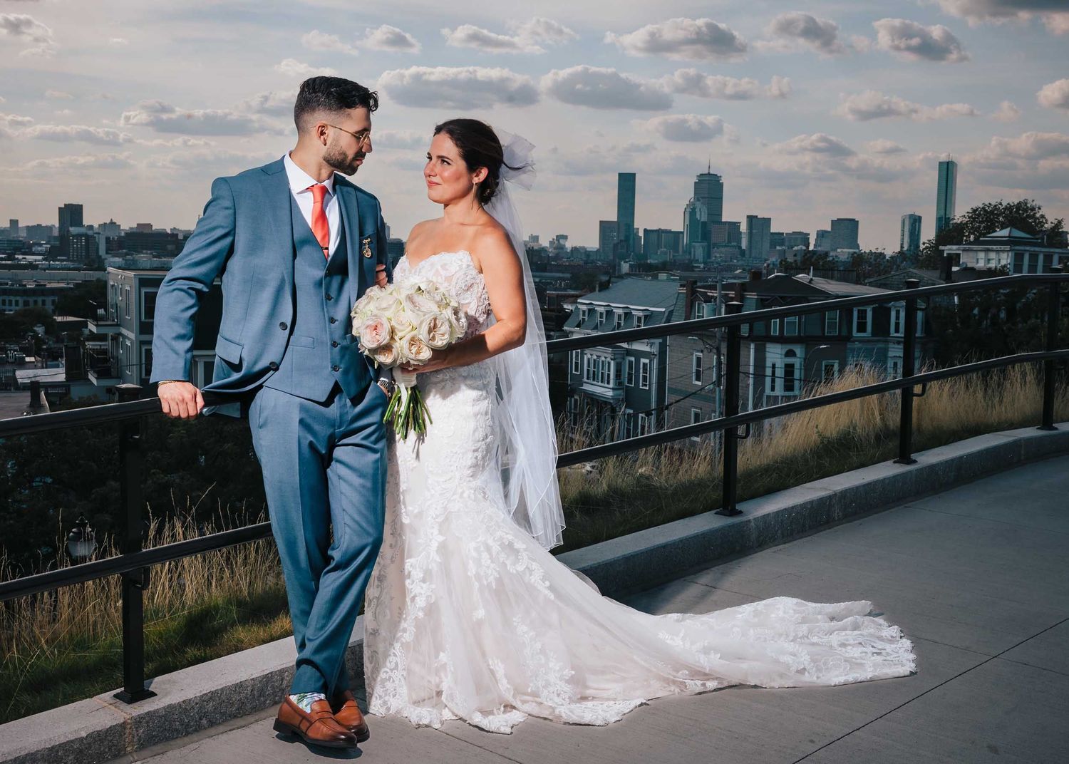 Bride and groom posing for wedding portraits at Dorchester Heights with the Boston skyline in the background